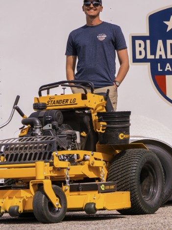 Blade Runner Lawn Care owner standing on a stand-on mower in front of the branded trailer